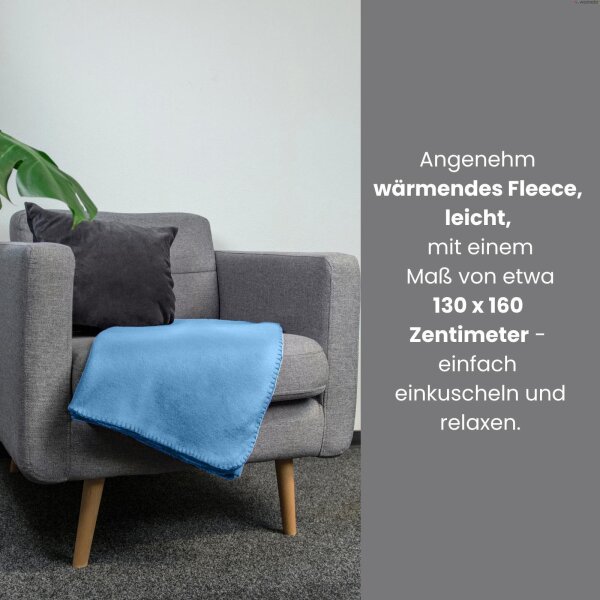 Eine blaue Fleecedecke liegt elegant auf einem hellgrauen Sitzmöbel zusammen mit einem schwarzen Samtkissen.