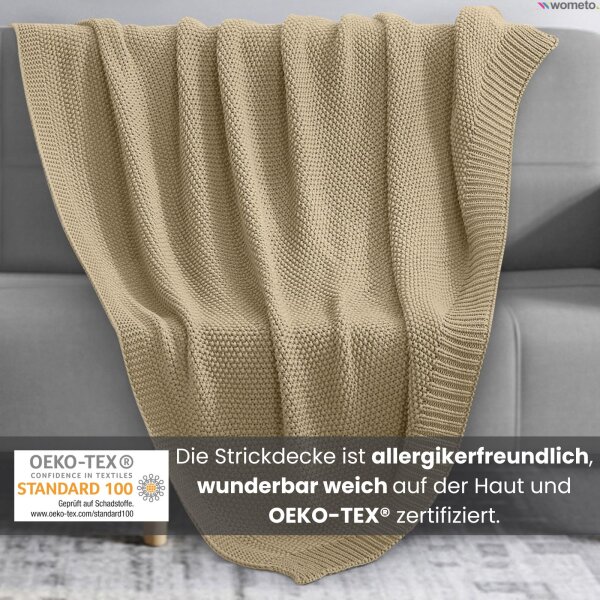 Eine Strickdecke in der Farbe Beige liegt über der Couch. Darunter der Hinweis, die Kuscheldecke ist allergikerfreundlich.