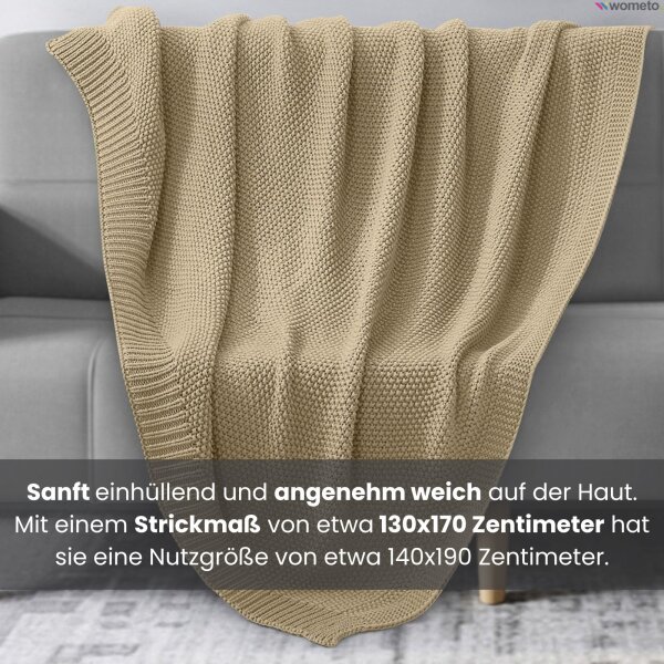 Eine beige Strickdecke liegt auf einer Couch. Sie hat eine Nutzgröße von 140x190 Zentimeter.