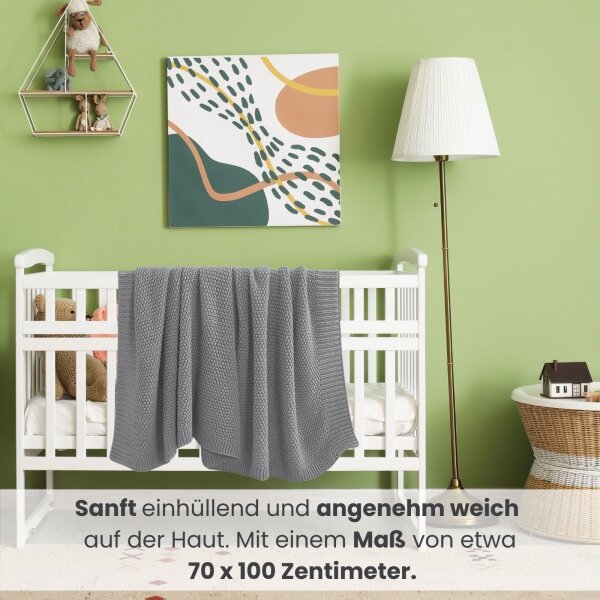 Im bunten Kinderzimmer hängt eine graue Strickdecke über dem Babybett.